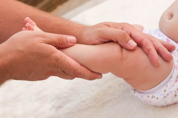 Mains qui massent jambes de bébé