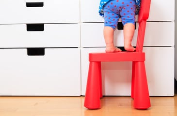 Jambes de bébé debout sur petite chaise rouge